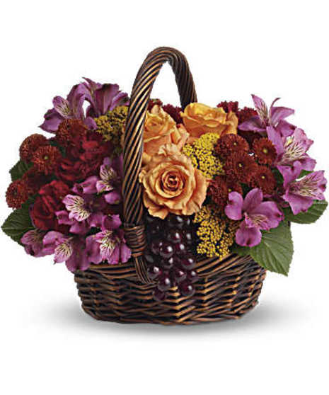 A dark, handled basket delivers a mix of orange roses, maroon carnations, purple alstroemeria, burgundy button mums and yellow yarrow
