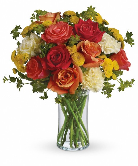 Dark orange, orange and coral roses are gathered with light yellow carnations, yellow button mums and fresh green bupleurum and pittosporum in a simple glass gathering vase