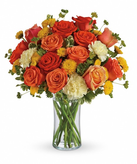 Dark orange, orange and coral roses are gathered with light yellow carnations, yellow button mums and fresh green bupleurum and pittosporum in a simple glass gathering vase